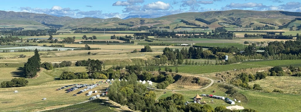 Scenic view of a rural landscape with fields, trees, and mountains under a blue sky.